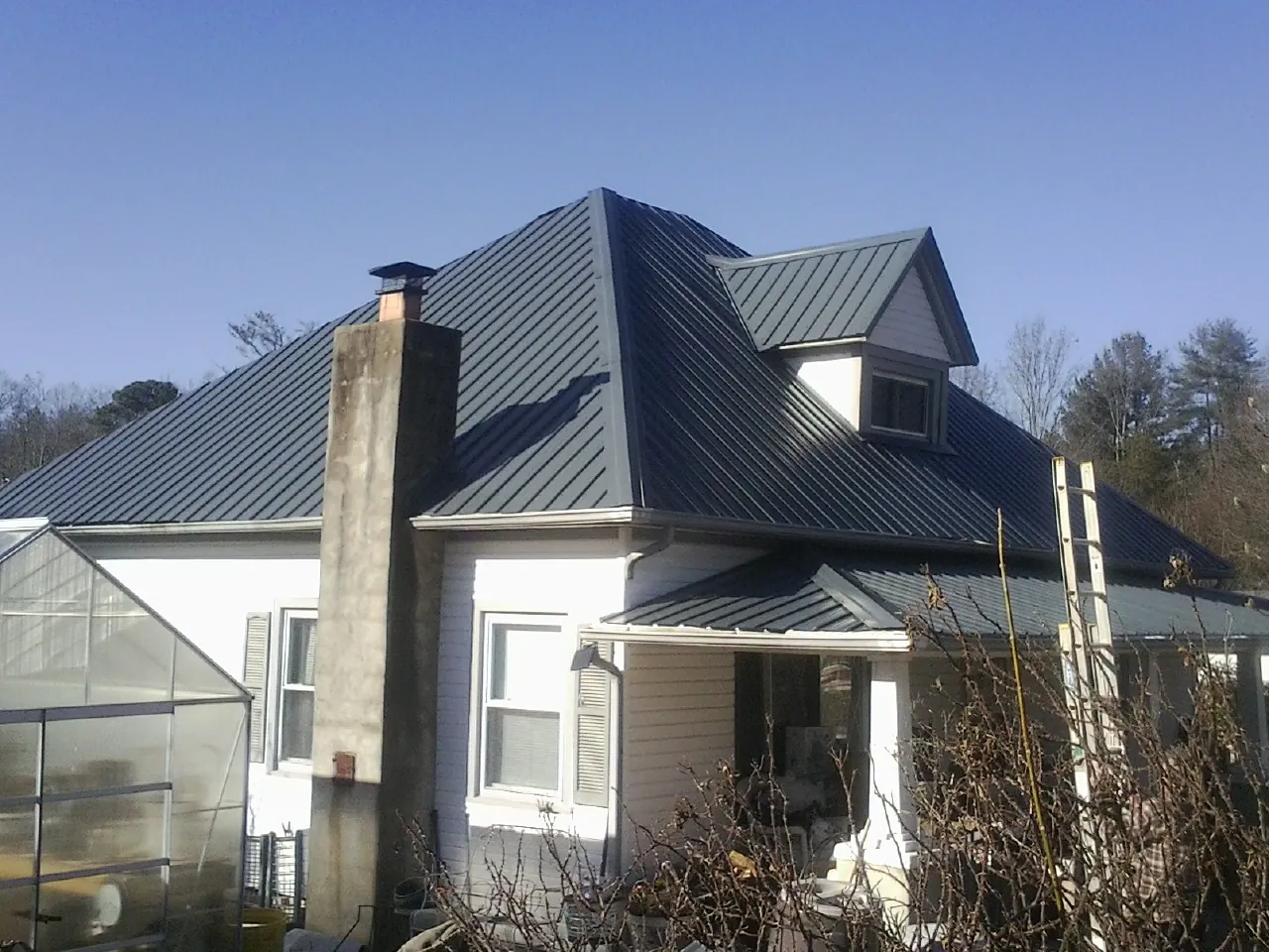 Dark blue standing seam metal roof on a white farmhouse with dormer — Slate & Tile Roof Repair by Roofing Brothers in Larchmont