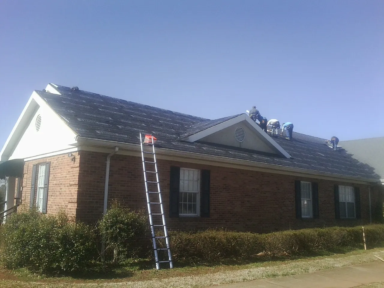 Crew tearing shingles off a brick ranch roof with a ladder set — Metal Roof Repair work by our crew in Larchmont