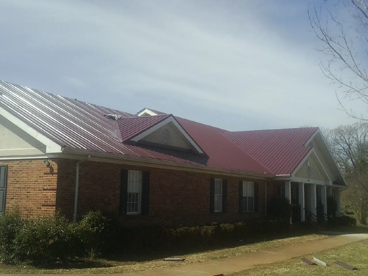 Red metal roof with gabled entries on a long brick building, from a Hail Damage Roof Repair job in Larchmont