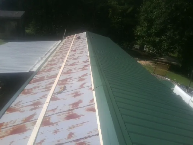 Old rusted panels beside newly installed green metal roofing — Wind Damage Roof Repair by Roofing Brothers in Larchmont