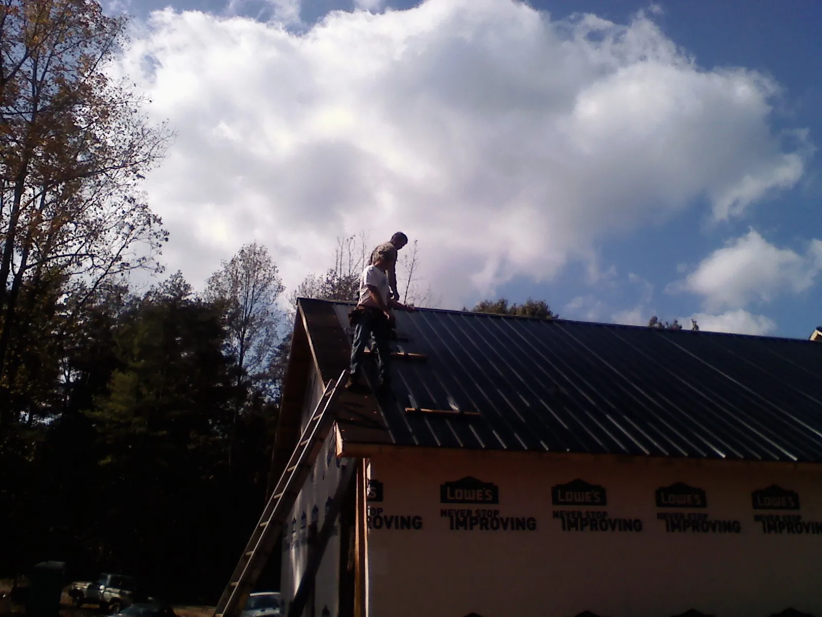 Roofer fastening dark metal panels high against a cloudy sky, from a Roof Inspection job in Larchmont