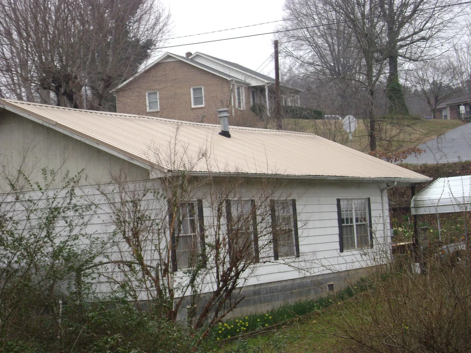 Tan metal roof on a white sided house set into a hillside — Commercial Roofing by Roofing Brothers in Larchmont