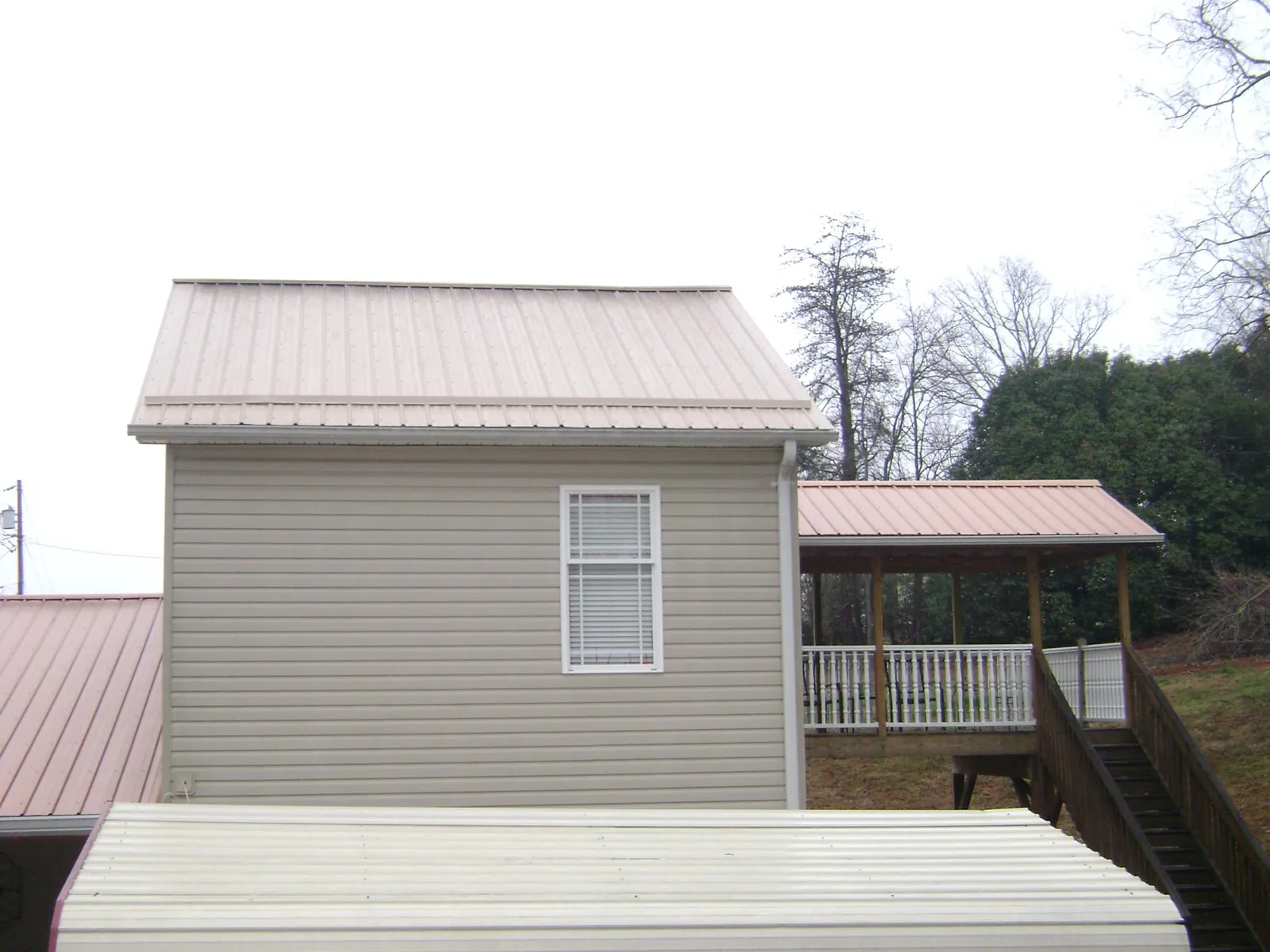 Tan metal roofs on a two story addition and attached porch, from a Roof Replacement job in Larchmont